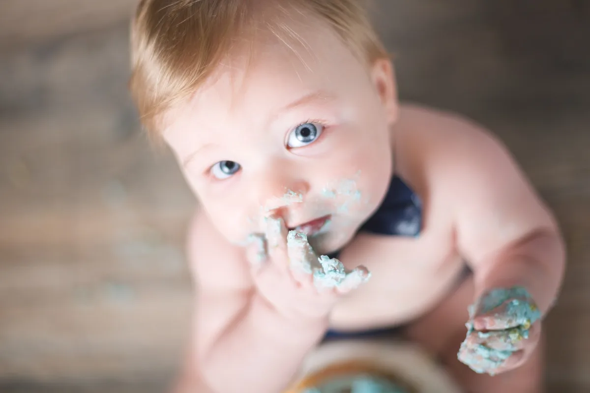 Baby boy with bow tie enjoying cake at home smash session