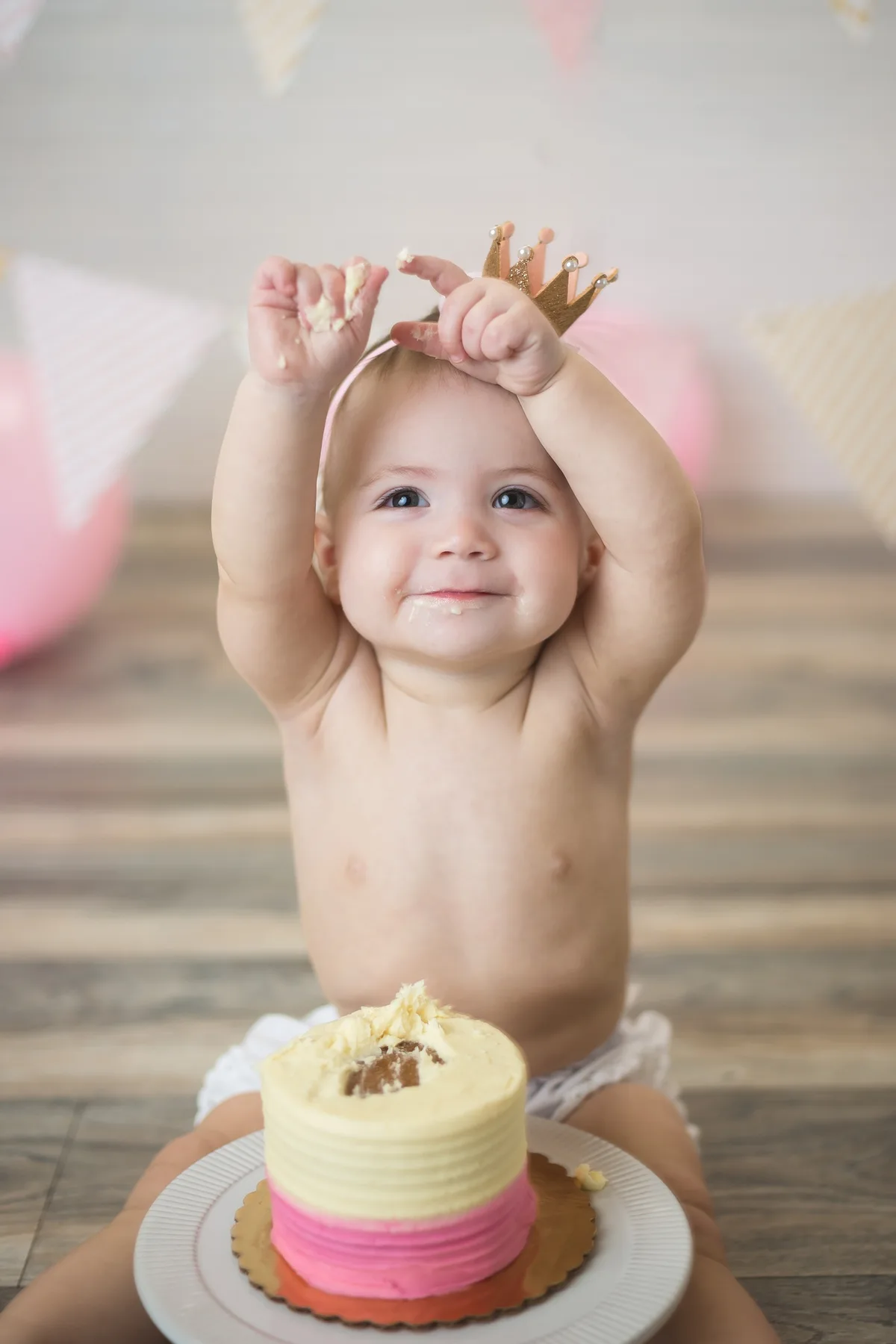 Baby with frosting all over hands and face, smiling during a cake smash session
