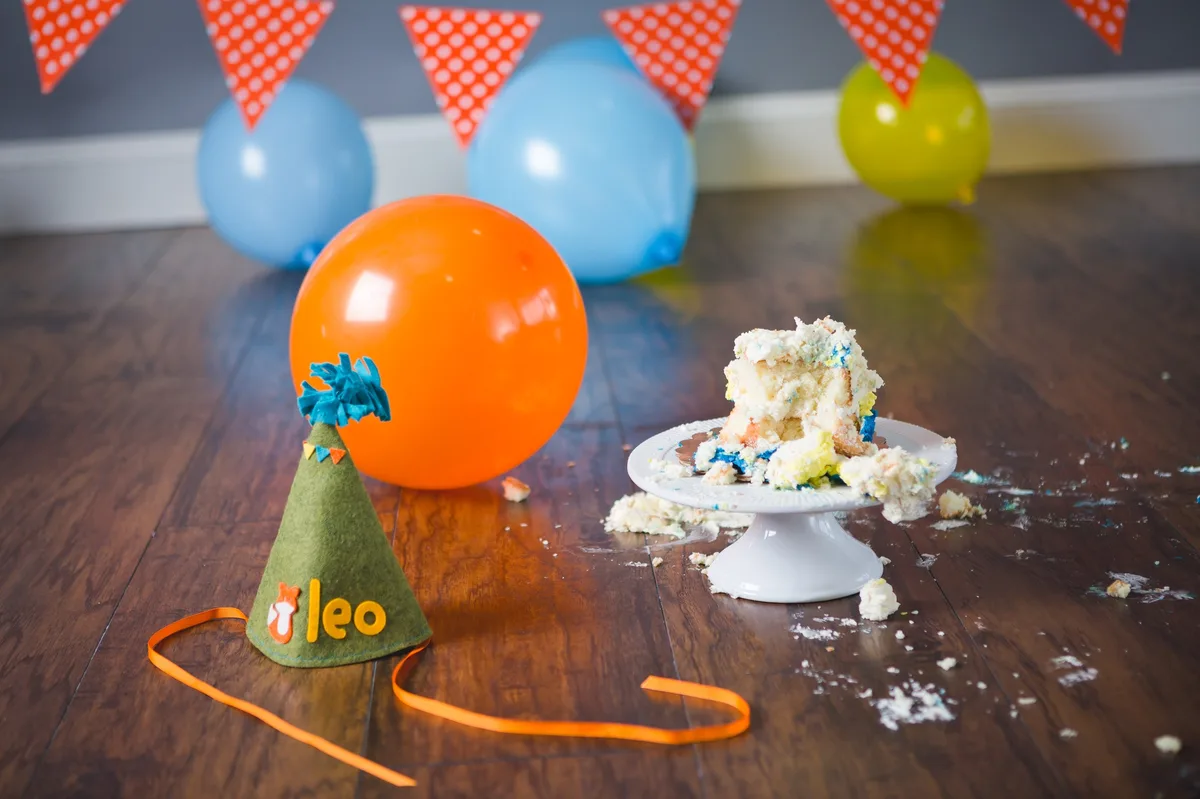 The aftermath of a cake smash session — destroyed cake, party hat, and crumbs on the studio floor