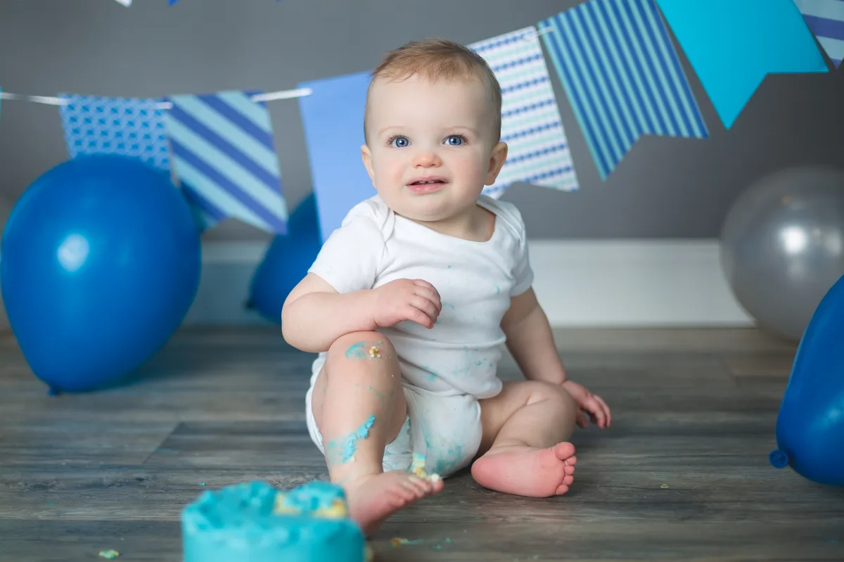 Baby with a blue smash cake, balloons, and number one sign at a Chicago cake smash photography studio