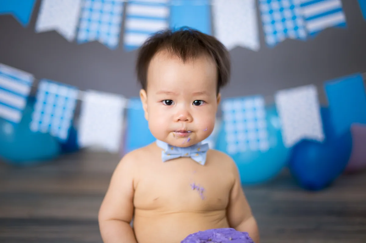 Baby with a purple smash cake, balloons, and birthday banner at a Chicago cake smash photography studio