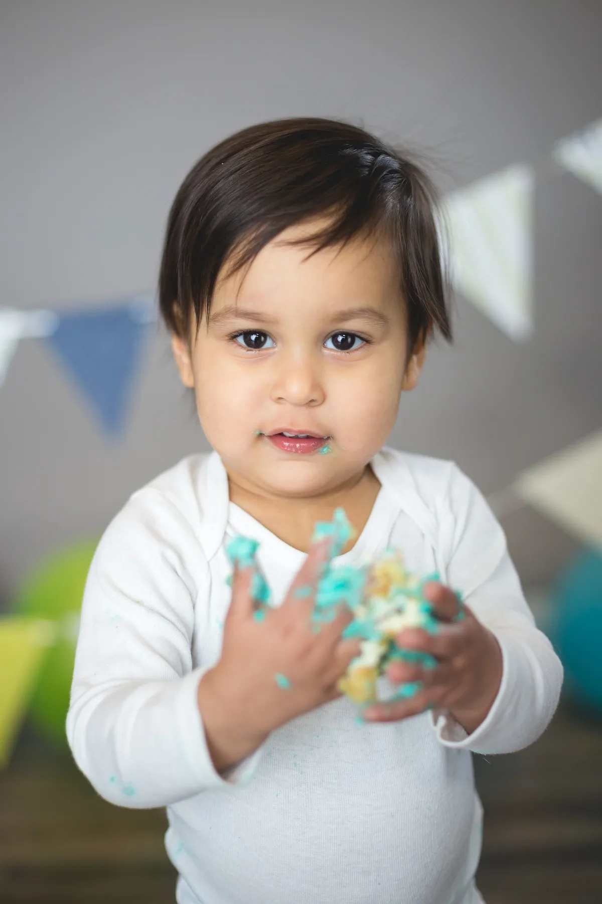 Baby playing with teal cake frosting during a first birthday cake smash photo session in Chicago
