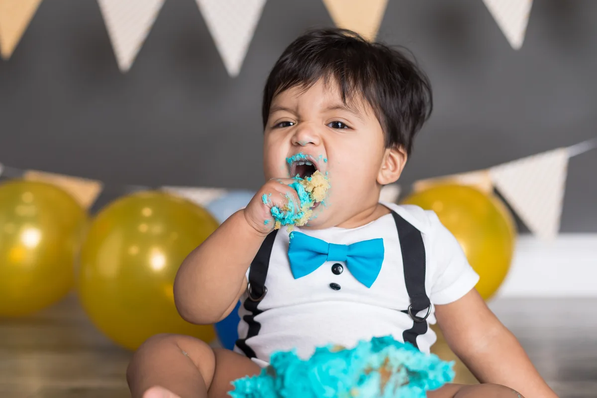 Boy in bow tie eating teal cake with frosting on face and hands