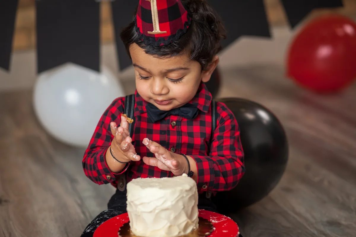 Baby in gold outfit smashing white frosted cake on elegant stand