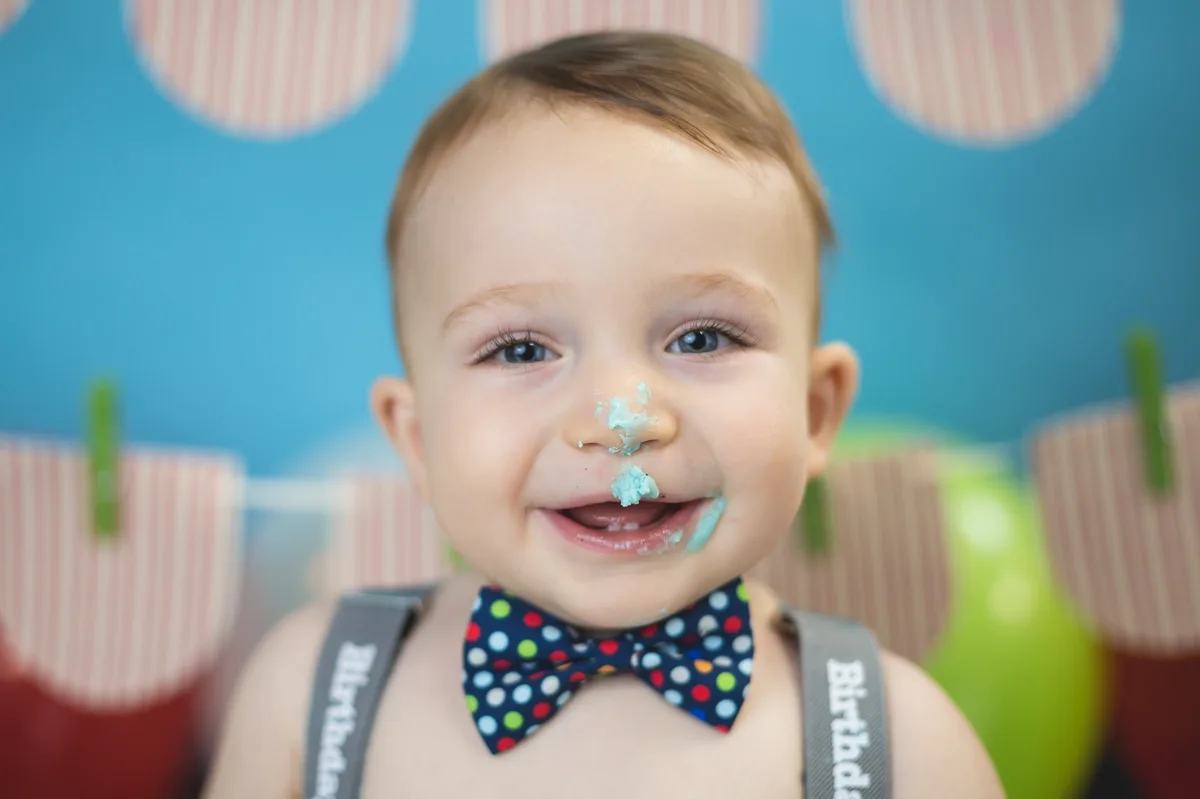 Joyful baby with teal frosting on hands during studio cake smash