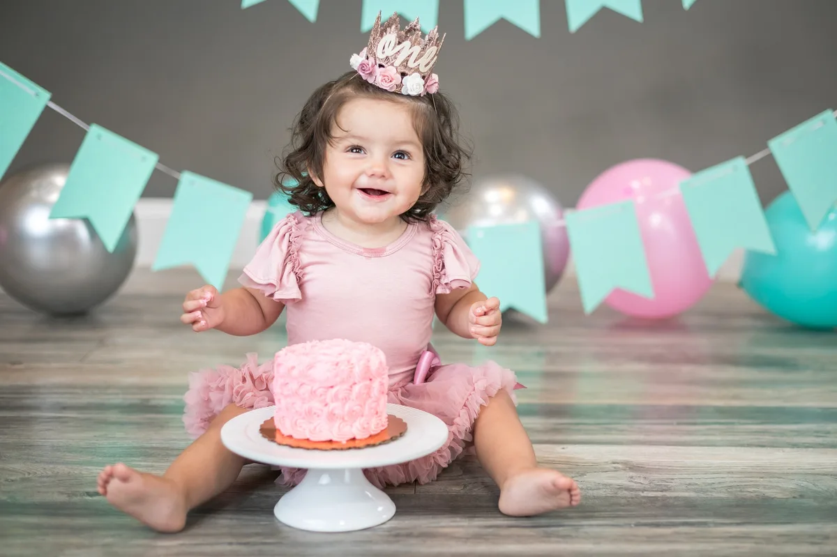 Baby girl in pink tutu with rosette smash cake on white cake stand